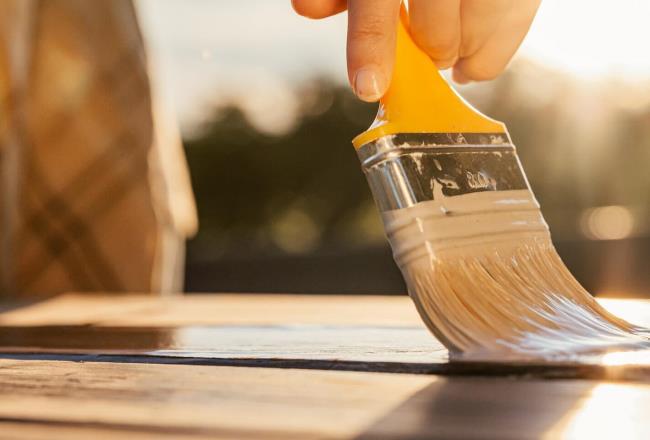 Person in lumberjack shirt painting outside with a small yellow brush