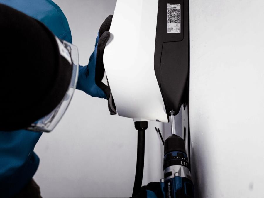 Technician installing a charging station to a white wall.