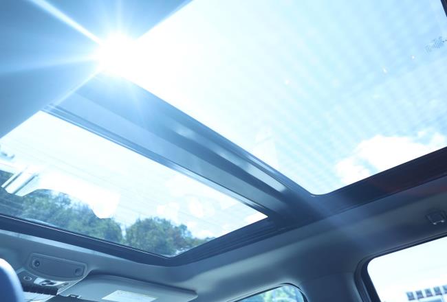 Car interior, looking up through a glass sunroof with sunshine streaming in.