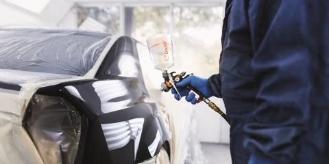 A man in overalls holds a Dockit capsule ready to apply clearcoat to a car exterior.