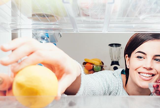 A woman reaching for fruit in her refrigerator.