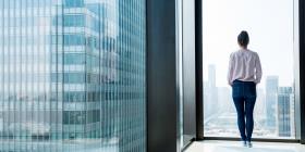 Woman looks out onto a city landscape through window in residential building