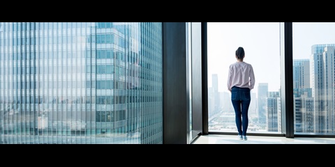 Woman looks out onto a city landscape through window in residential building
