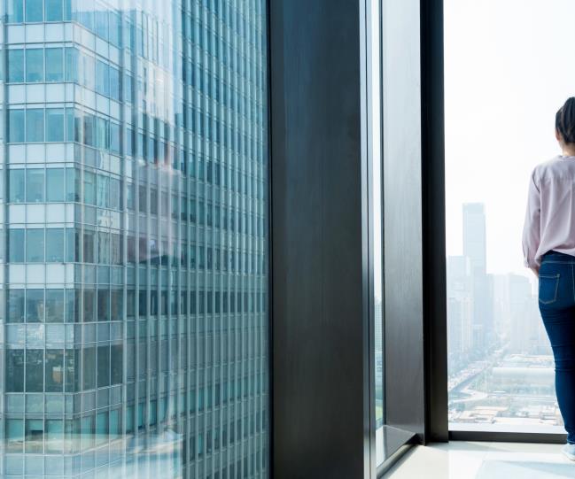 Woman looks out onto a city landscape through window in residential building