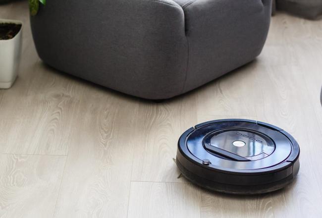 Robot vacuum cleaner navigates a wood floor surface between a fireplace and a sofa