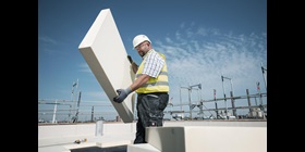 Construction worker on a building site holding a thick, rigid panel of PU insulation.