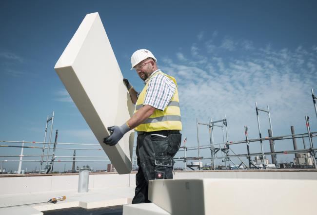 Construction worker on a building site holding a thick, rigid panel of PU insulation.
