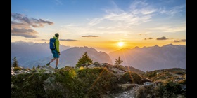 Ein Mann wandert bei Sonnenuntergang vor einem Bergpanorama