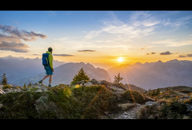 Ein Mann wandert bei Sonnenuntergang vor einem Bergpanorama