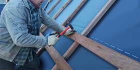 A craftsman hammers a nail into the crossbeam to fix it to the rafter