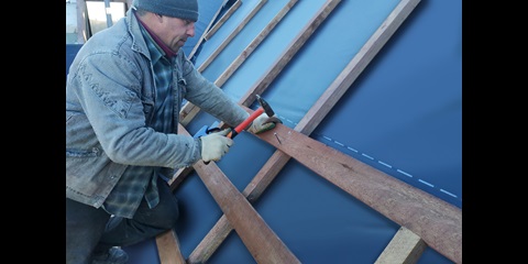 A craftsman hammers a nail into the crossbeam to fix it to the rafter