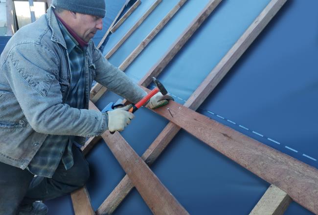 A craftsman hammers a nail into the crossbeam to fix it to the rafter