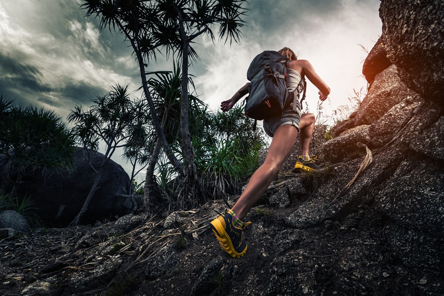 Woman hiker with backpack climbs steep rocky terrain