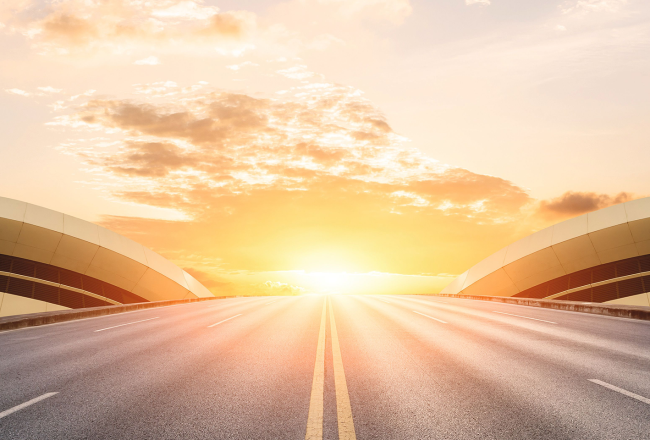 Asphalt road in front of modern bridge construction before sunset