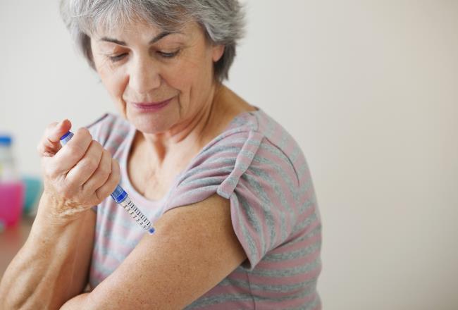 A woman injecting medicine to her upper arm.