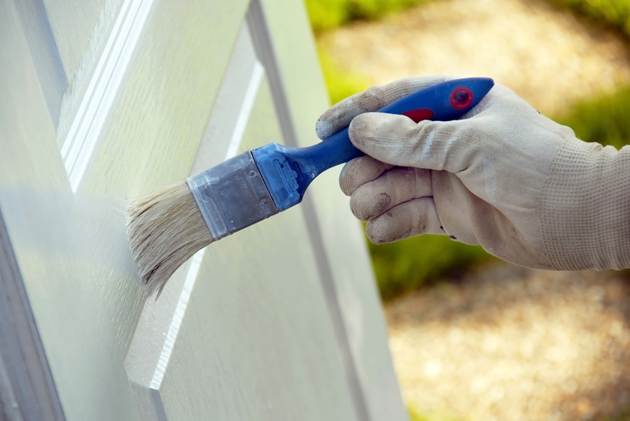 A white door being painted with a small brush by a hand wearing a white glove