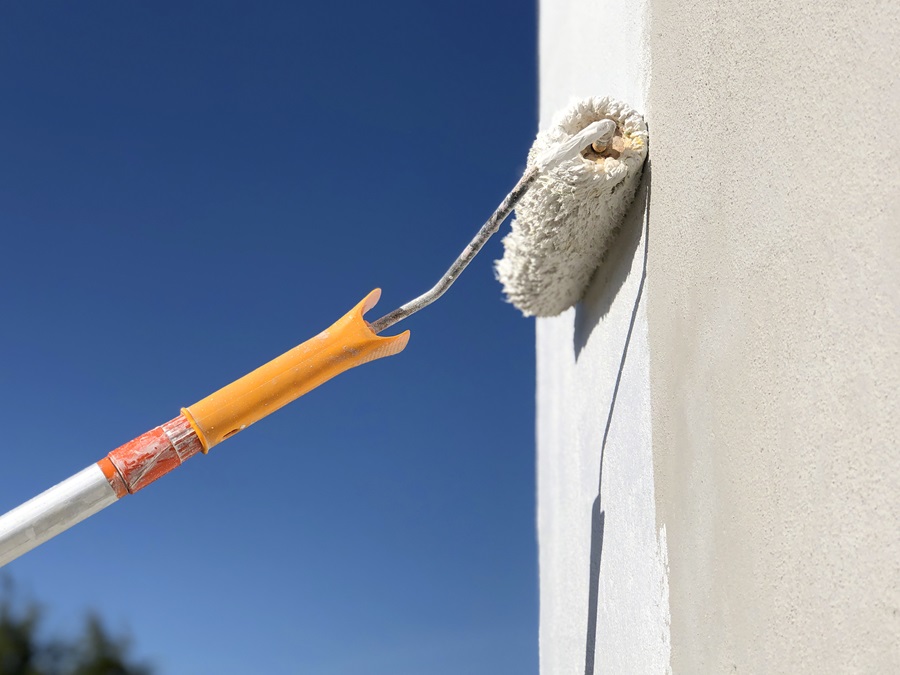 An exterior wall being painted with a big roller brush against a blue sky