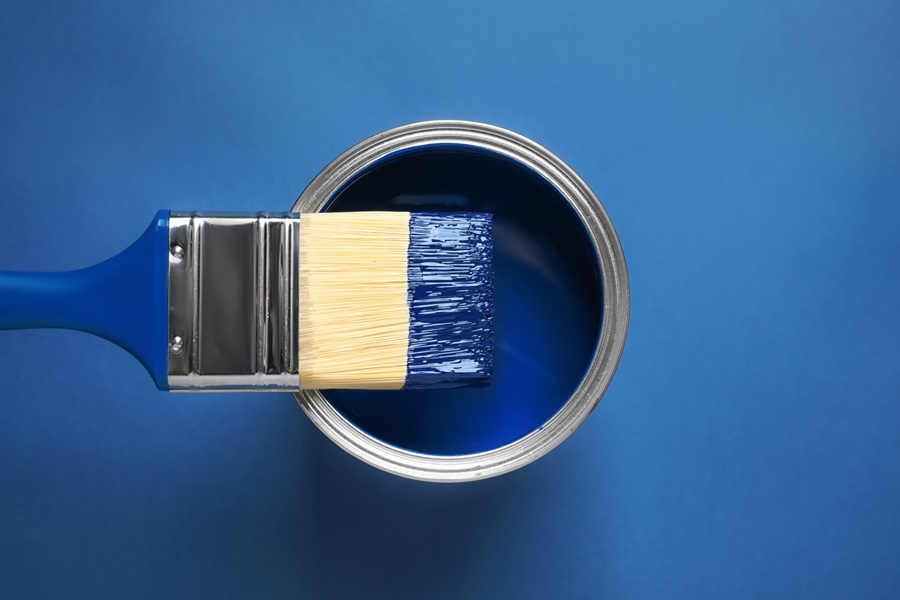 Bucket of blue paint with a brush dipped in paint lying on it, against a blue background