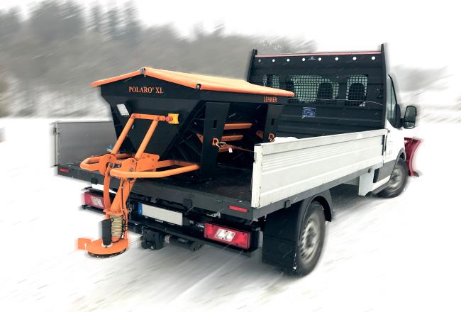 Small drop-side truck with a Lehner winter service salt spreader installed in the load bed.