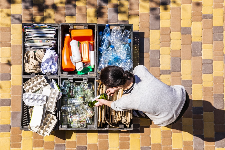 Woman sorting household recycling into hard and flexible plastic, glass, paper, and cardboard.