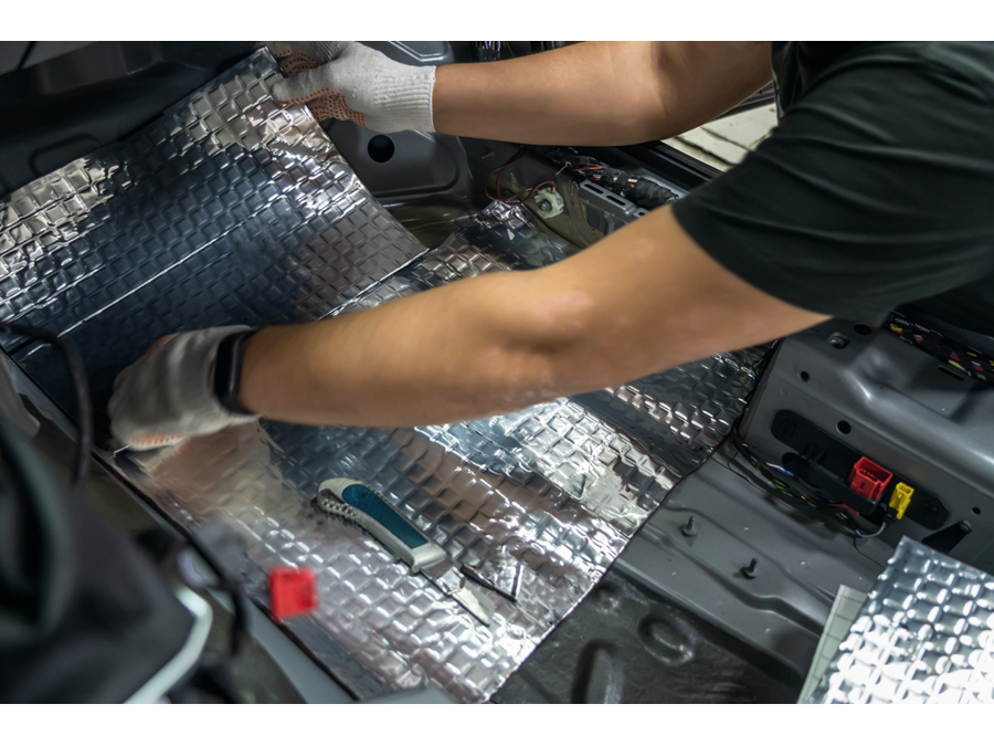 Worker hands glues soundproofing material to inside of car floor