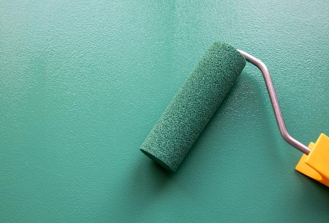 Paint roller with green color on painted wooden surface. Chalk board. Painting and renovation.