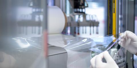 Pair of gloved hands holding a sheet of transparent ultrathin plastic film