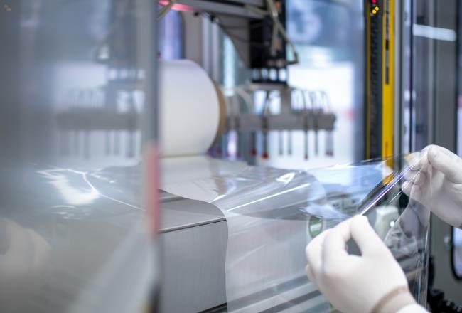 Pair of gloved hands holding a sheet of transparent ultrathin plastic film