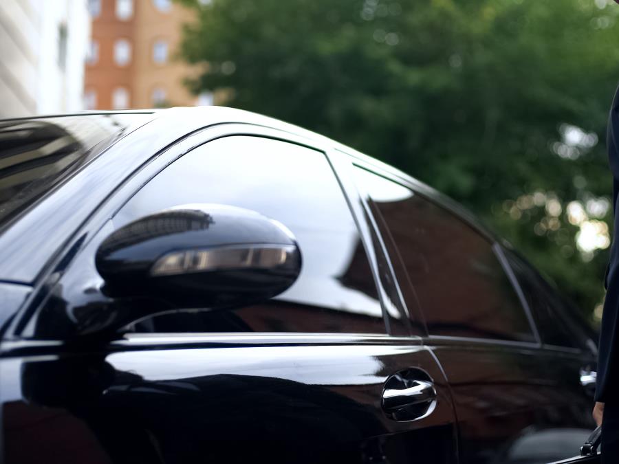 A man in a suit stands next to an armored limousine
