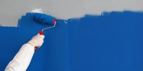 Close-up of adult painting wall with bright blue paint. Hand using roller for renovation work