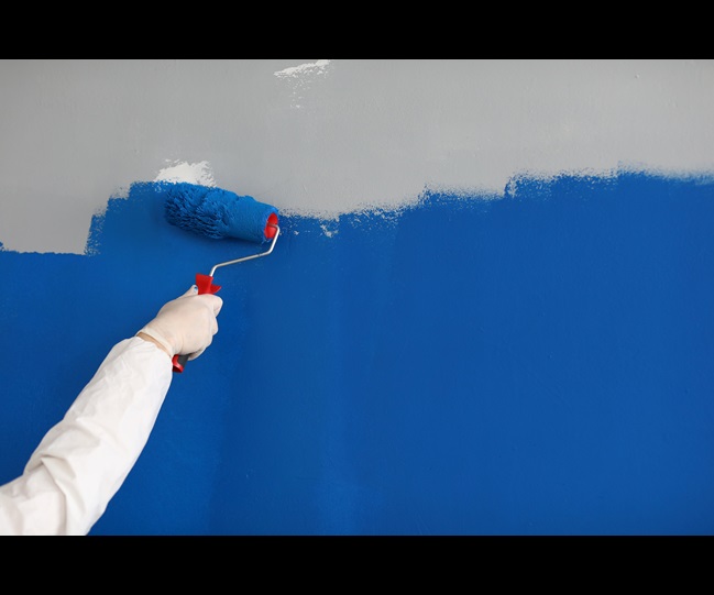 Close-up of adult painting wall with bright blue paint. Hand using roller for renovation work