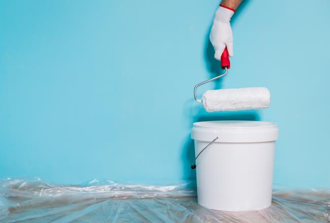 Image of paint can and man holding paint roller in front of blue wall.