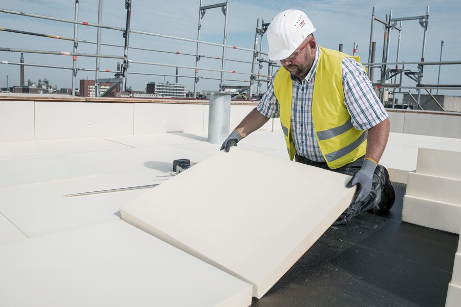 Hard-hatted construction worker placing a cut panel of rigid PU insulation on a building roof.