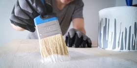 Close-up: brush with white paint on a wooden table and a jar with white paint