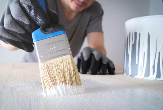 Close-up: brush with white paint on a wooden table and a jar with white paint