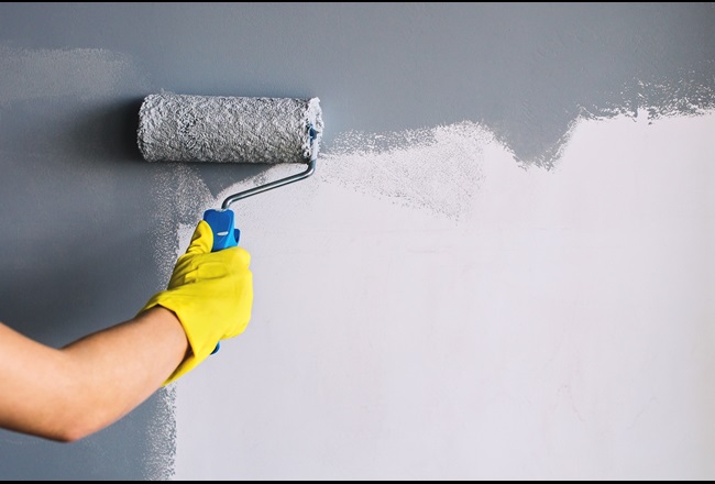 Hand in yellow glove painting wall in gray color with a roller brush.