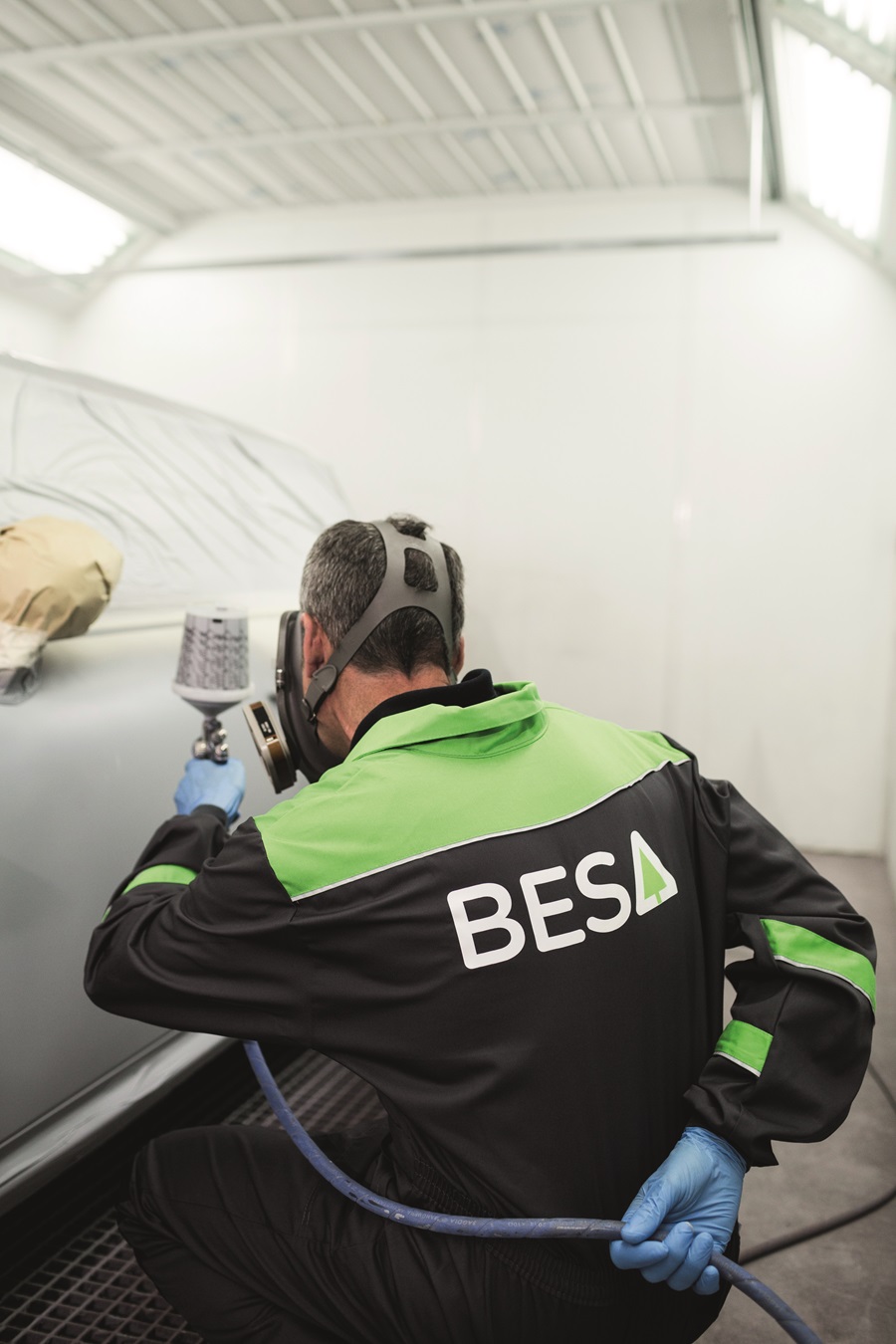 A man working in automotive exterior refinishing spray-painting a car.