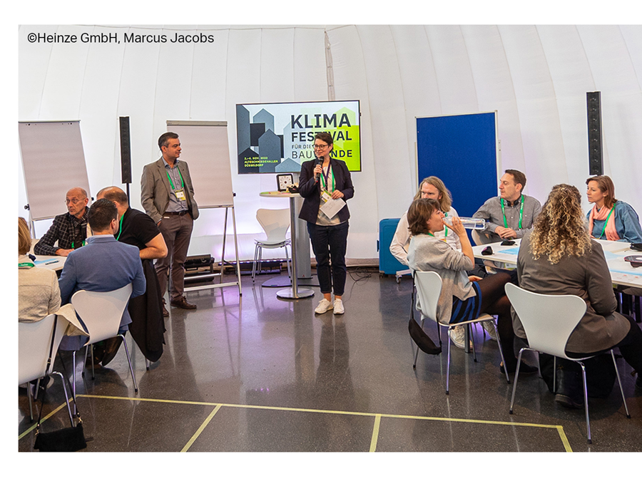 View of workshop with moderator and multiple tables of participants.